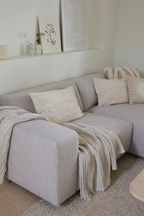 Ljusgrå hörnsoffa med beige kuddar och filtar i modernt vardagsrum med minimalistisk inredning