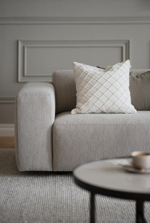 Beige bouclésofa med vit rutmönstrad kudde i elegant vardagsrum med grå väggar