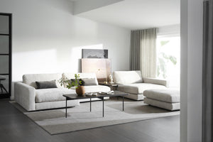 Ljust vardagsrum med grå modulsoffa, svarta soffbord och minimalistisk inredning i neutrala toner