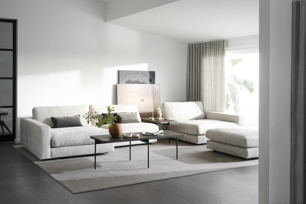 Ljust vardagsrum med grå modulsoffa, svarta soffbord och minimalistisk inredning i neutrala toner