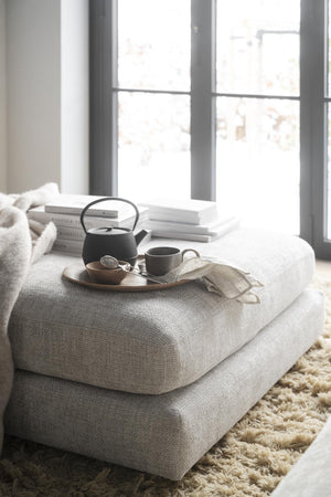 Mysig läshörna med tepanna, kopp och böcker på ljus ottoman vid fönster med naturligt ljus