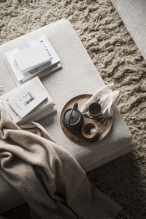 Mysig hemmiljö med tepanna, kopp och arkitekturmagasin på ljus kudde över luggmatta