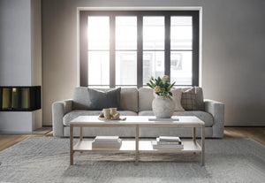 Minimalistiskt vardagsrum med grå soffa, vitt soffbord i metall och stort fönster med naturligt ljus