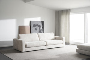 Vit modulsoffa i minimalistiskt vardagsrum med grå matta och stora fönster