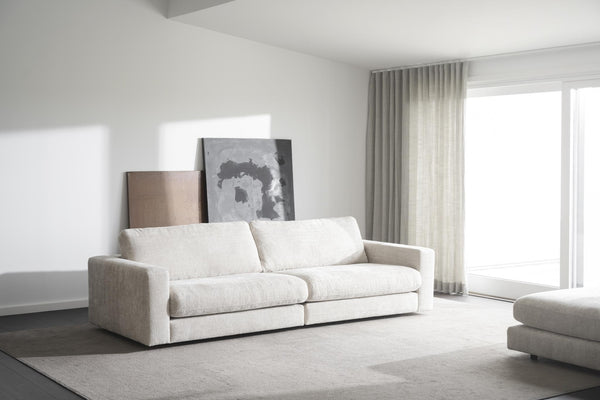 Vit modulsoffa i minimalistiskt vardagsrum med grå matta och stora fönster