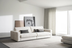 Vit modulsoffa med grå kuddar i minimalistiskt vardagsrum med stor fönstervägg och konstverk