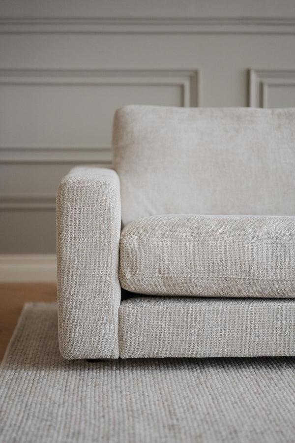 Beige soffa med kuddöverdrag i linnetyg mot ljus vägg med stuckatur