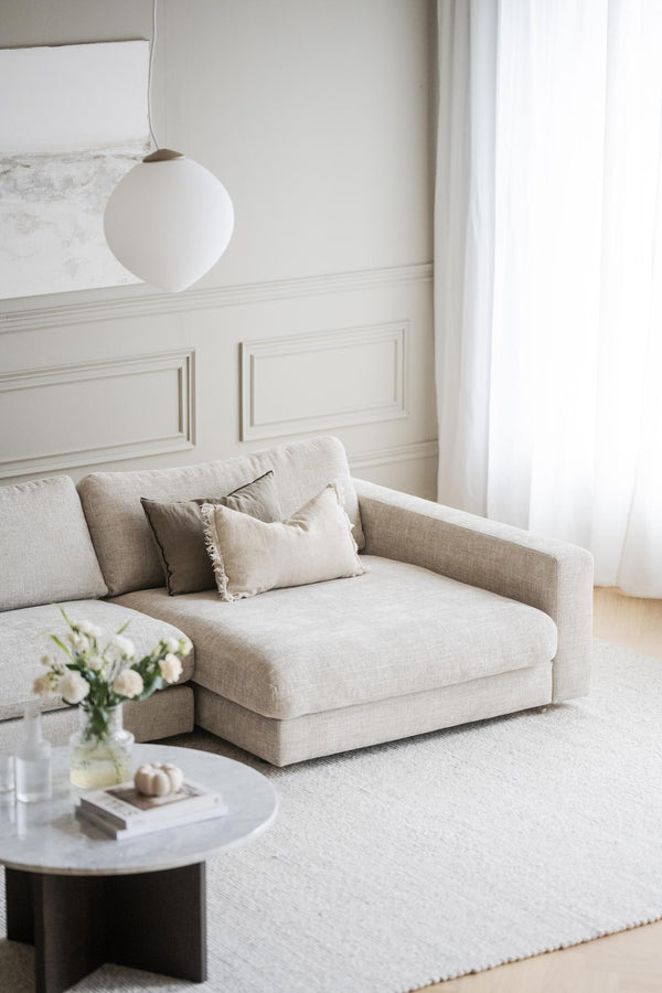 Ljust vardagsrum med beige lädersoffa, rund vit taklampa, marmorbord och vita väggar med spegelpaneler