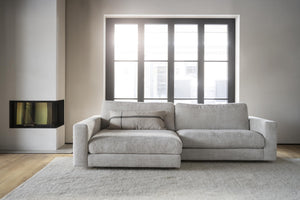 Grå soffa med schäslong i modernt vardagsrum med stor fönstervägg och öppen spis