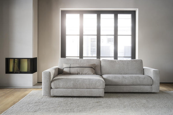 Grå soffa med schäslong i modernt vardagsrum med stor fönstervägg och öppen spis