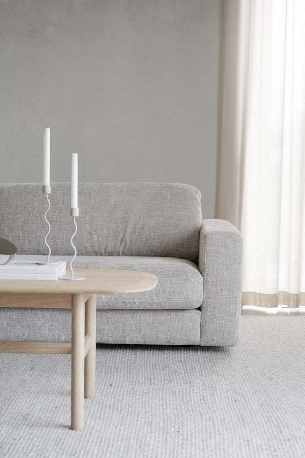 Minimalistiskt vardagsrum med grå soffa, ljust soffbord i trä och vita ljusstakar på vit matta