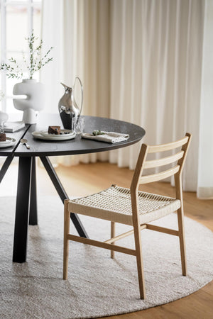 Ljus trässtol med flätad sits vid svart runt matbord i skandinavisk matsal med beige matta