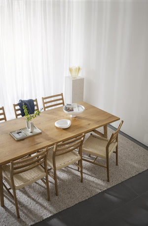 Matbord i massiv ek med sex stolar med rotting omgivet av vita väggar och textilgardiner i modern skandinavisk matsal