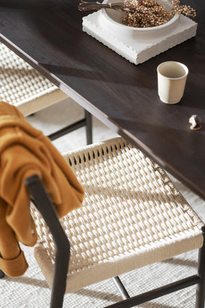 Matbord i mörkt trä med flätad stol i rotting och beige textilier i skandinavisk inredningsstil