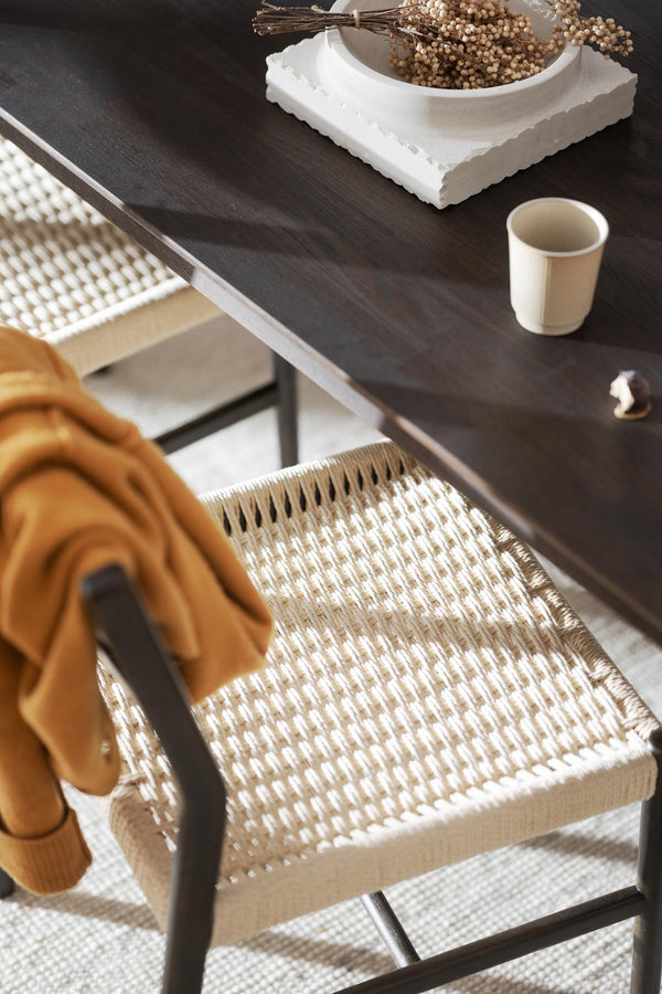 Matbord i mörkt trä med flätad stol i rotting och beige textilier i skandinavisk inredningsstil