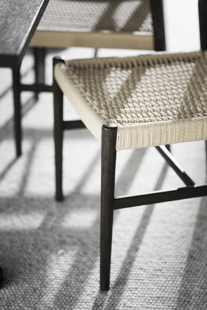 Närbild på stol med flätad sits i naturfiber och svartbetsade träben på ljus matta