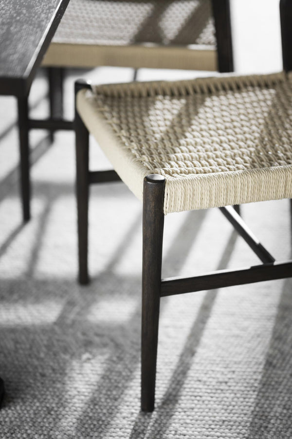 Närbild på stol med flätad sits i naturfiber och svartbetsade träben på ljus matta