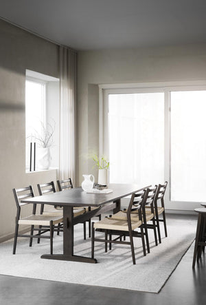 Matbord i mörkt trä med sex stolar i skandinavisk stil i minimalistiskt matrum med stora fönster
