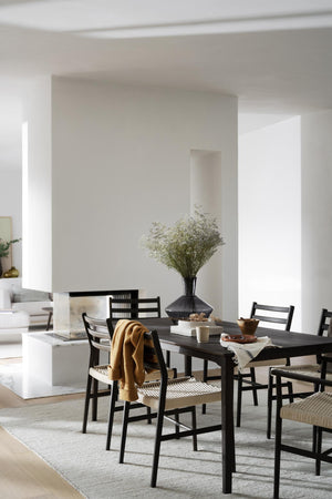 Matbord i svart trä med stolar i skandinavisk design, dekorerat med vas och duk i minimalistiskt hem