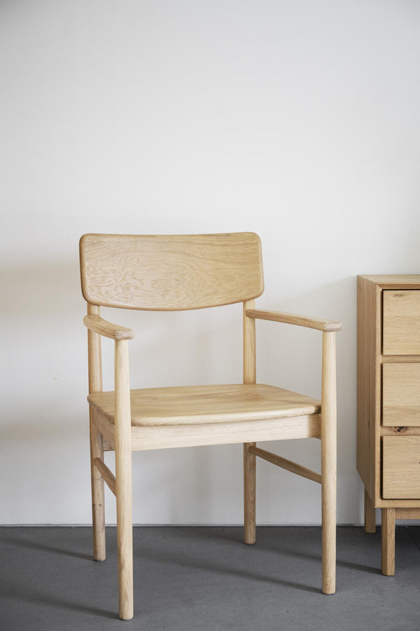 Stol i ljust trä med armstöd och ryggstöd, skandinavisk design, bredvid byrå mot vit vägg