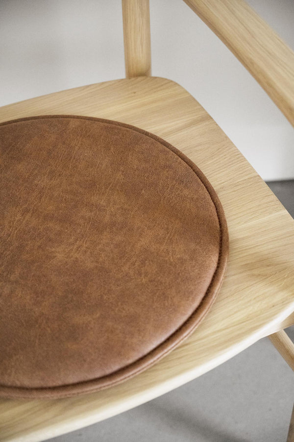 Närbild av stol i ljust trä med brun mockasits, visar sits och ryggstöd i minimalistisk design