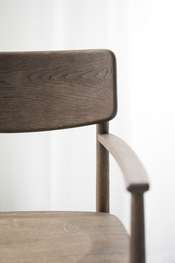 Närbild på stol i mörk ek med rundade former och synlig trästruktur mot vit bakgrund