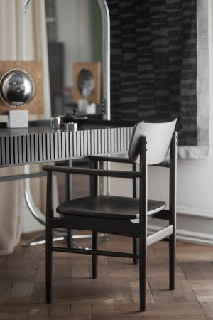 Svart stol med armstöd framför spegel och skåp med räfflad front i modernt inrederat rum