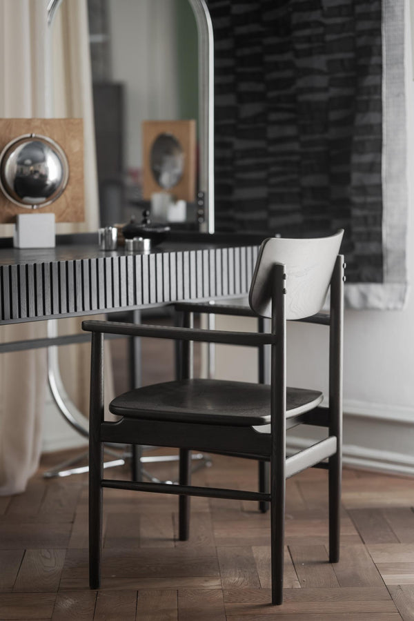 Svart stol med armstöd framför spegel och skåp med räfflad front i modernt inrederat rum