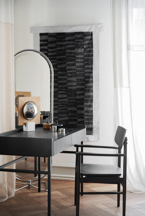 Svart skrivbord med rillad front och spegel, matchande stol vid öppen spis med svart tegelvägg