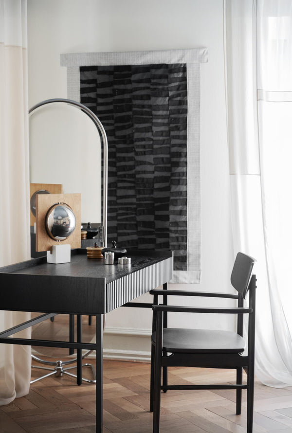 Svart skrivbord med rillad front och spegel, matchande stol vid öppen spis med svart tegelvägg