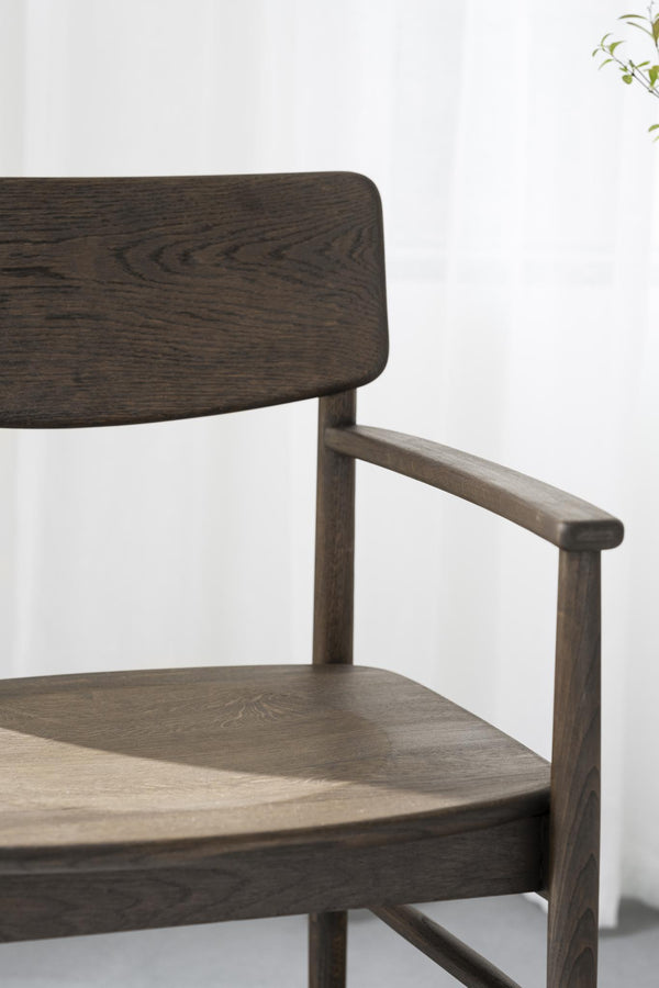 Närbild på mörkbrun träfåtölj med armstöd och elegant träsits i skandinavisk design