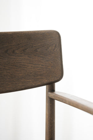 Närbild av mörk ekstol med rundade hörn och naturlig trästruktur, eleganta träben