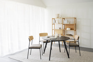 Matbord med stolar i skandinavisk design med ljust trä och svarta ben, kombinerat med öppen hylla i bakgrunden