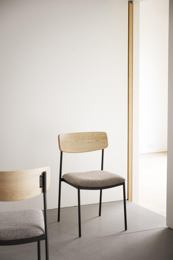 Matstol med ljust trä ryggstöd, grå stoppad sits och svarta metallben i minimalistisk inredning