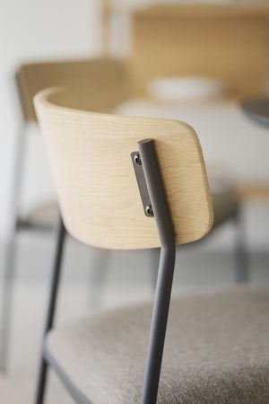 Närbild på ljus trärygg och grå metallben på modern stol med minimalistisk design