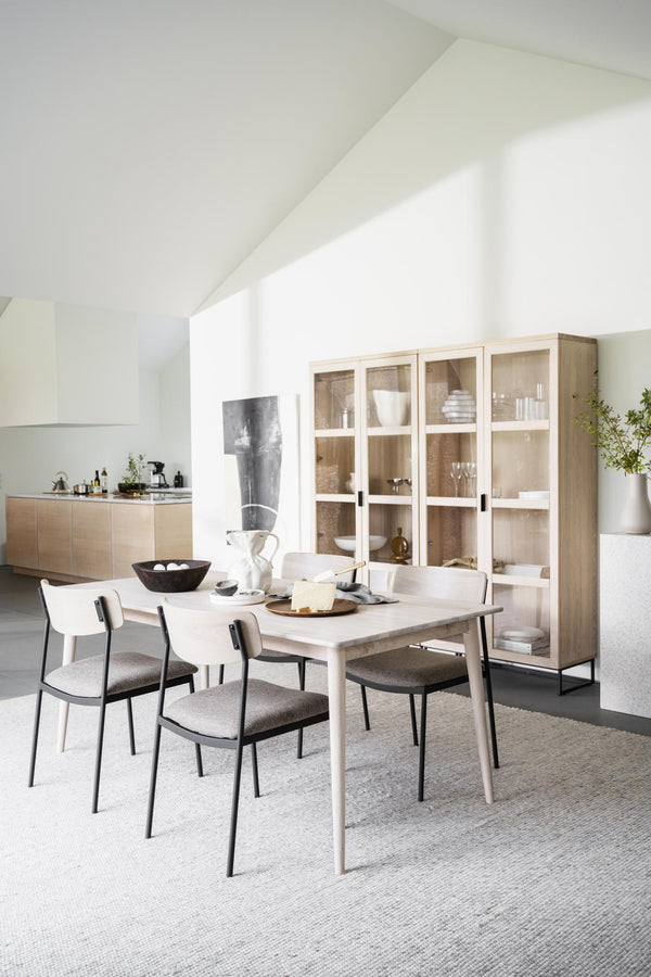 Ljus matplats med ljust träbord, stolar med grå dynor och vitrinskåp i skandinavisk design