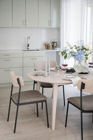 Ljust kök med runt matbord i trä och stolar med grå dynor, dekorerat med blommor och ljusstakar