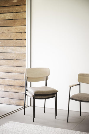 Moderna matstolar med ljust trä och beige sits på svart metallstativ framför vit vägg och träpanel
