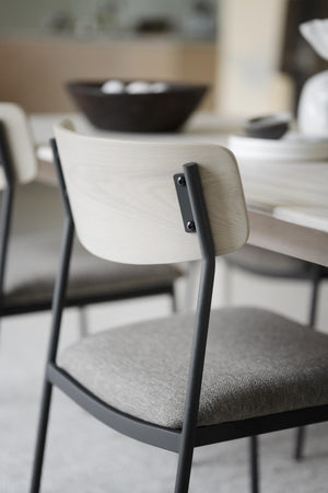 Matstol med ljus trärygg och grå dyna vid matbord, skandinavisk design med svarta metallben