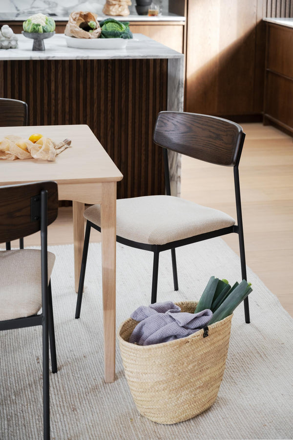 Matstol med beige stoppad sits, mörkbrun trärygg och svarta metallben vid matbord i modern skandinavisk stil