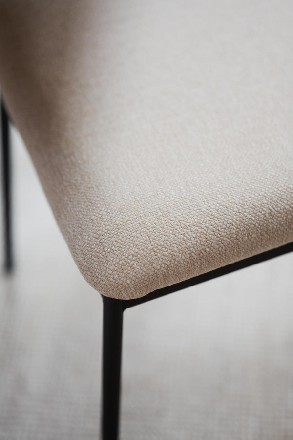 Närbild på beige stoppat sits med textilytrå och svart metallram på modern matstol