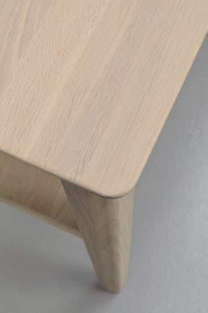 Närbild på träbordsskiva med ljus ekfärg och rundade hörn, visar naturlig trästruktur och fot i massivt trä