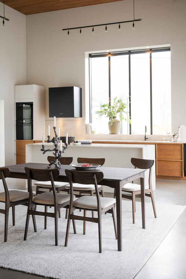 Matplats med grå matbord och stolar i mörkt trä med ljusa dynor, integrerat kök med trädetaljer i bakgrunden