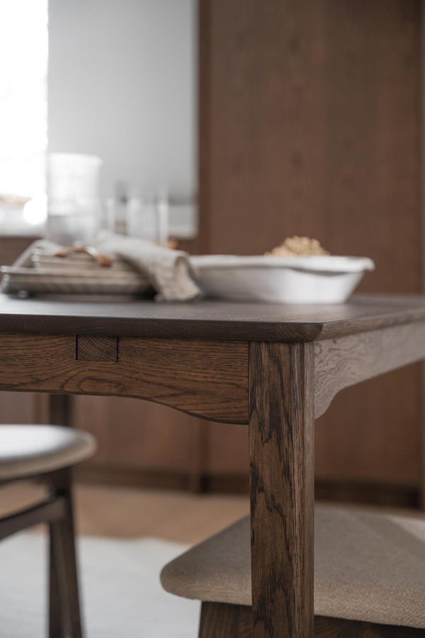 Massivt matbord i mörk ek med synlig trästruktur och träben, med dukade skålar och tallrikar