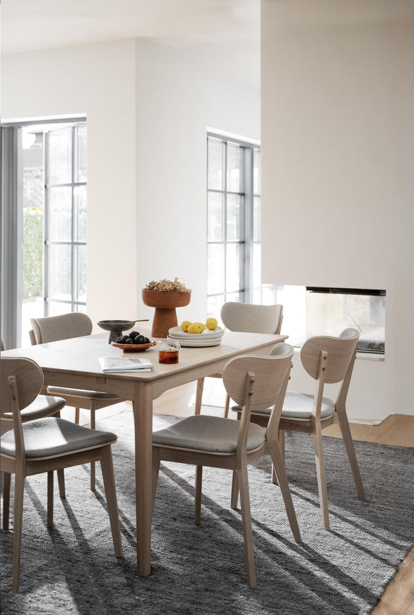 Matgrupp i ljust trä med sex stolar och grå dynor i minimalistisk matsal med stora fönster