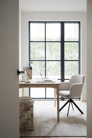 Minimalistiskt hemmakontor med ljust träskrivbord, grå kontorsstol och stora industrifönster med svarta spröjs
