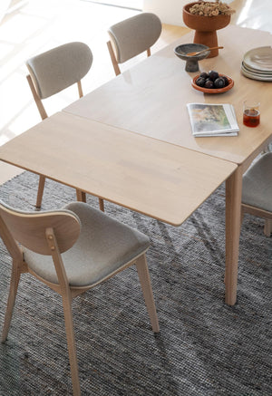 Ljust matbord i trä med grå stoppade stolar på vävd matta, dekorerat med keramik och tillbehör