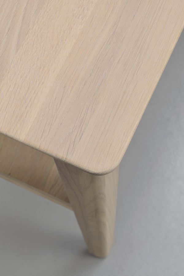 Närbild på träbordsskiva med synlig trästruktur och rundad kant, samt bordsben i ljust trä