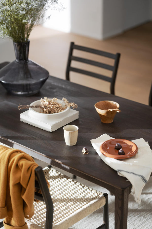 Mörkt matbord med keramikskålar, kopp och dekorationer i jordnära färger med stolar i rotting och svart trä