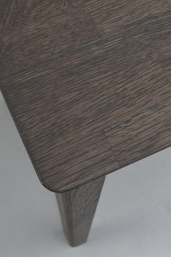 Mörkbrun träbordsskiva med synlig faneråder och avsmalnande träben i närbild